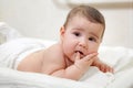 Warried Caucasian baby lying on his stomach with fingers in mouth, looking at camera Royalty Free Stock Photo