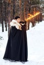 A warrior in black quilted clothes in a black cloak with a white fur collar and a long fiery sword in his hands