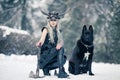 Warrior woman in image of viking with ax and horned helmet next to the big black dog in winter forest Royalty Free Stock Photo