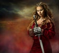 Warrior Woman praying with Sword. Medieval Female Knight in Armor blessing Battle. Beautiful Viking Girl in Red Fantasy Dress over Royalty Free Stock Photo