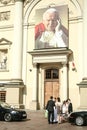 newly married young people standing in front of a church with a giant picture of John Paul II,