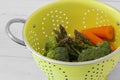 Washed asparagus, broccoli and carrot vegetables in a bright green colander strainer.