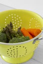 Washed asparagus, broccoli and carrot vegetables in a bright green colander strainer.