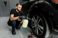 Washing a car in detailing service. Indoor shot of male worker in uniform, washing the car wheels rims with pressure