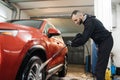 Close up of red car wheel indoor. Smiling bearded man washing red car with water jet. Royalty Free Stock Photo