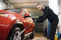 Close up of red car wheel indoor. Smiling bearded man washing red car with water jet. Royalty Free Stock Photo