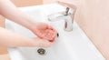 Washing femle hands in white ceramic washbasin with a chrome faucet.