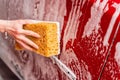 Washing a red car with a foamy yellow sponge. Woman& x27;s hand washing a car at the car wash Royalty Free Stock Photo