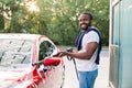 Washing of red modern car on open air self car wash service with foam and high powered hose. Young smiling African man Royalty Free Stock Photo