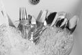 Washing silver spoons, forks and knives under stream of water in kitchen sink, closeup Royalty Free Stock Photo