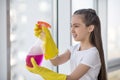 Teenager girl splashing cleanser on the window.