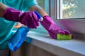 Washing windows. Female hands in gloves hold spray bottle with glass cleaner and sponge. woman washes window and sill in room Royalty Free Stock Photo