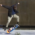 A young bearded caucasian man wearing baseball hat, canvas pants and a thin coat is doing a 360 rotation with his skateboard.