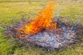 Waste incineration at the summer cottage. Flames from dry burning branches on the field, burnt ashes. Danger of handling fire Royalty Free Stock Photo