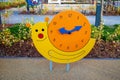 The watch face is wooden with yellow hands on a wooden board with a beautiful snail pattern in a city park