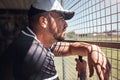 When we watch, we learn. a young man watching a game of baseball from behind the fence.