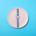 Watch with time six o`clock on a white plate on a blue background. Concept of limiting the intake of food diet and Royalty Free Stock Photo