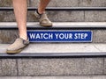 Watch your step sign on a staircase and a pair of feet