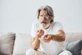 Watches interesting TV show. Senior stylish modern man with grey hair and beard indoors Royalty Free Stock Photo