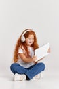 Watching cartoons. Cute redheaded little girl wearing tee and jeans using tablet isolated over white studio background