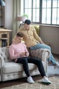 Man in orange shirt sitting on the sofa watching his partner chatting online