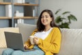 Watching movie or chatting on social networks. Positive arab woman with laptop and cup of tea or coffee resting on sofa Royalty Free Stock Photo