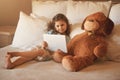 Watching a movie with my best friend. an adorable little girl at home watching a movie on a tablet with her teddybear on