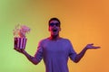 Portrait of Latina young man in 3d glasses holding bucket of popcorn isolated on gradient yellow green background in Royalty Free Stock Photo