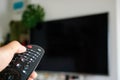 Watching Television Concept. Hand using a remote control in front of the TV screen. Relaxation in Modern Living Room. Focus on Royalty Free Stock Photo