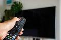 Watching Television Concept. Hand using a remote control in front of the TV screen. Relaxation in Modern Living Room. Focus on Royalty Free Stock Photo