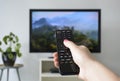 Watching TV. A woman`s hand holding the TV remote control with a television in the background Royalty Free Stock Photo