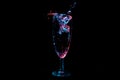 Clear liquid being poured into a tall clear glass under blue and red lights isolated on a black background Royalty Free Stock Photo