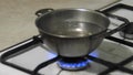 Bowl of water warmed on a dirty old gas stove at home. Water is boiling in a metal pot, close up. Poverty destitution