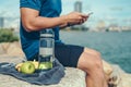 Water bottle, banana, earphone, green apple and towel on the ground beside young man rest after exercise and playing mobile phone Royalty Free Stock Photo