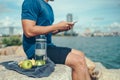 Water bottle, banana, earphone, green apple and towel on the ground beside young man rest after exercise and playing mobile phone Royalty Free Stock Photo