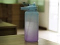 Water Bottle cylindrical with light blue-purple drinking straws placed on a wooden table Royalty Free Stock Photo