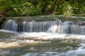 Water cascading over rocks in a woodland stream, sunlight and shade with heavy foliage Royalty Free Stock Photo