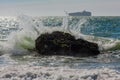 Water crashing into rock with boat in background