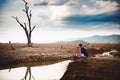 Hopeless and lonely farmer sit on cracked earth near drying water Royalty Free Stock Photo