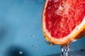 Water drips from half a grapefruit. Splashes and drops fly from a piece of grapefruit symbolizing the brightness and freshness of Royalty Free Stock Photo