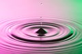 Water drop close with concentric ripples on colourful pink and green surface