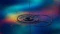 Water drop creating ripples on an iridescent colorful surface with bokeh splash liquid Royalty Free Stock Photo