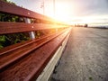 Water droplets on a wooden long bench by a side walk and rising sun with flare in the background. Selective focus. Calm and cool Royalty Free Stock Photo