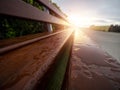 Water droplets on a wooden long bench by a side walk and rising sun with flare in the background. Selective focus. Calm and cool Royalty Free Stock Photo