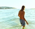 The water feels perfect. Rearview shot of a handsome young man standing in the water at the beach.