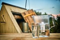 Water filter jug and a transparent glass cup of clean water in front of wooden draw well outdoors in summer evening