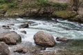 Water flow at small shallow mountain river at summer day. Stones stick out of the clear water. Close up