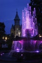 Water flowing from an artesian fountain decorated with colorful lights and a cathedral in the background. Royalty Free Stock Photo