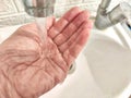 Water Flowing Onto an Open Hand in a Sink. detailed view of a stream of clear water pouring down onto the palm of a hand