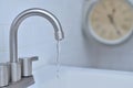 Water flowing out of a faucet, there is a clock in background.